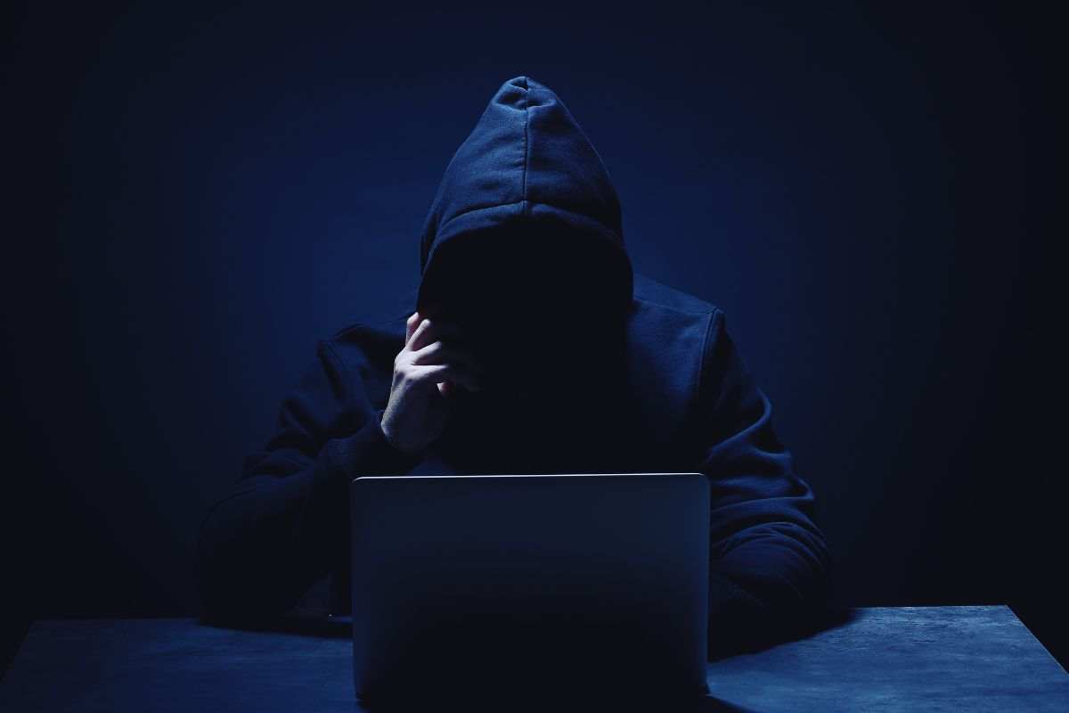 Hacker con viso nascosto da cappuccio che utilizza computer portatile