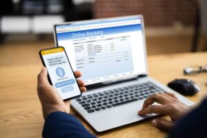 uomo con smartphone di fronte a home banking su pc