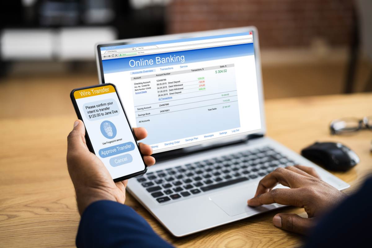 uomo con smartphone di fronte a home banking su pc